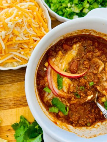 Partially eaten thick homemade chili in a bowl with cilantro, onions, cheese, and sour cream.