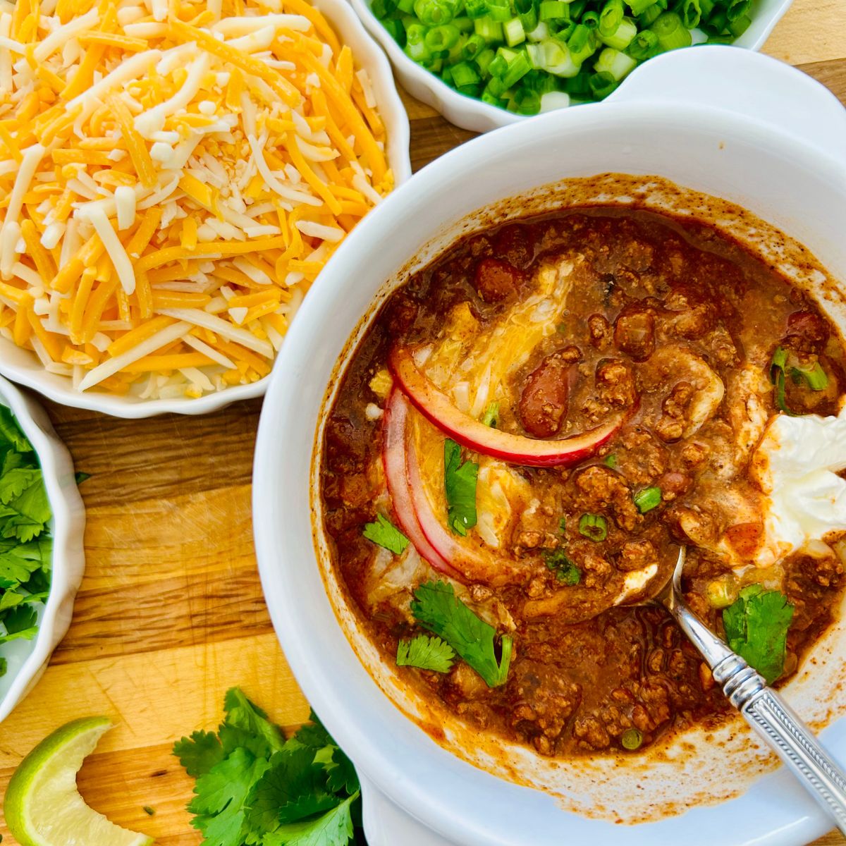 Partially eaten thick homemade chili in a bowl with cilantro, onions, cheese, and sour cream.