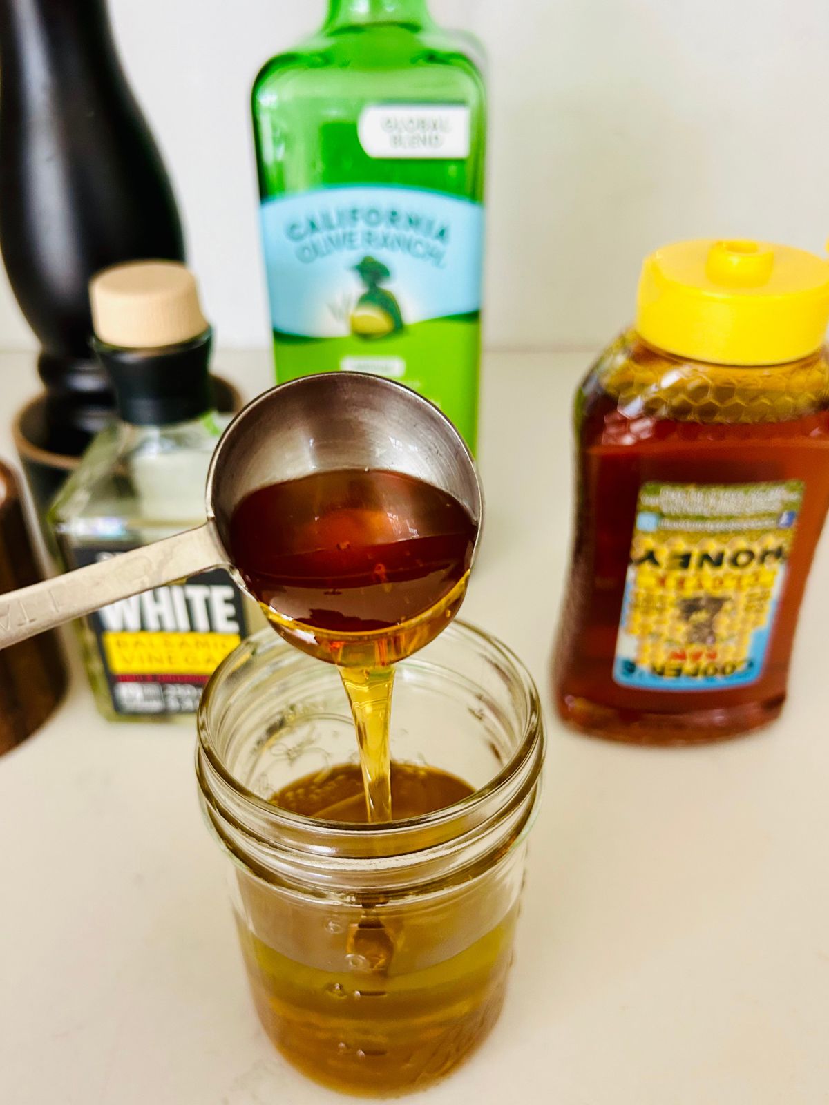 Pouring honey from a tablespoon into the mason jar full of olive oil.