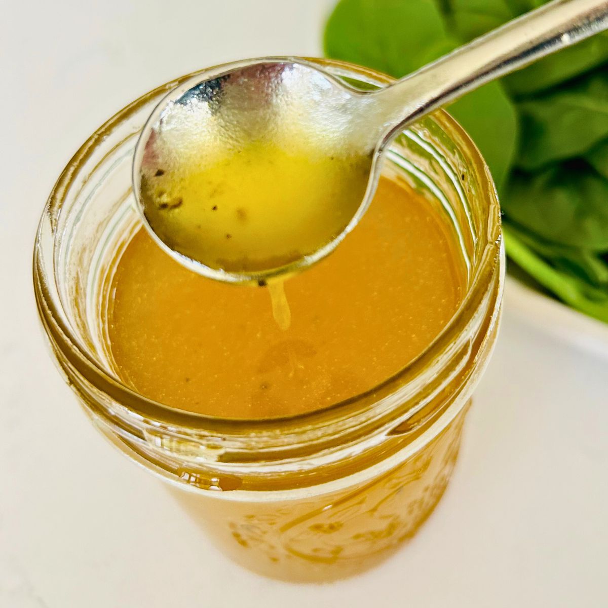 White balsamic vinaigrette dropping out of a spoon into the mason jar.