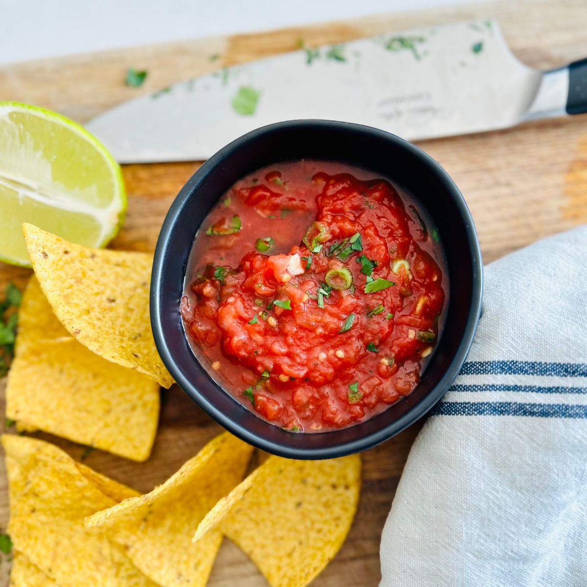 Red restaurant style salsa made from canned tomatoes in a black bowl next to tortilla chips.