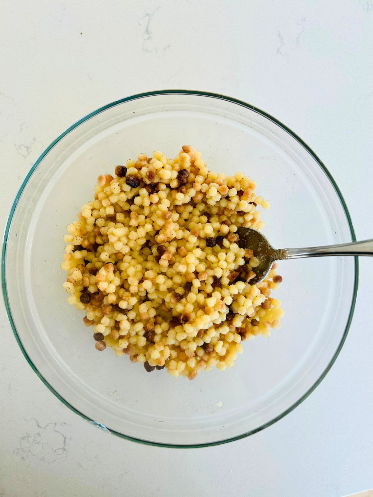 Cooked fregola pasta dressed with olive oil in a glass bowl.