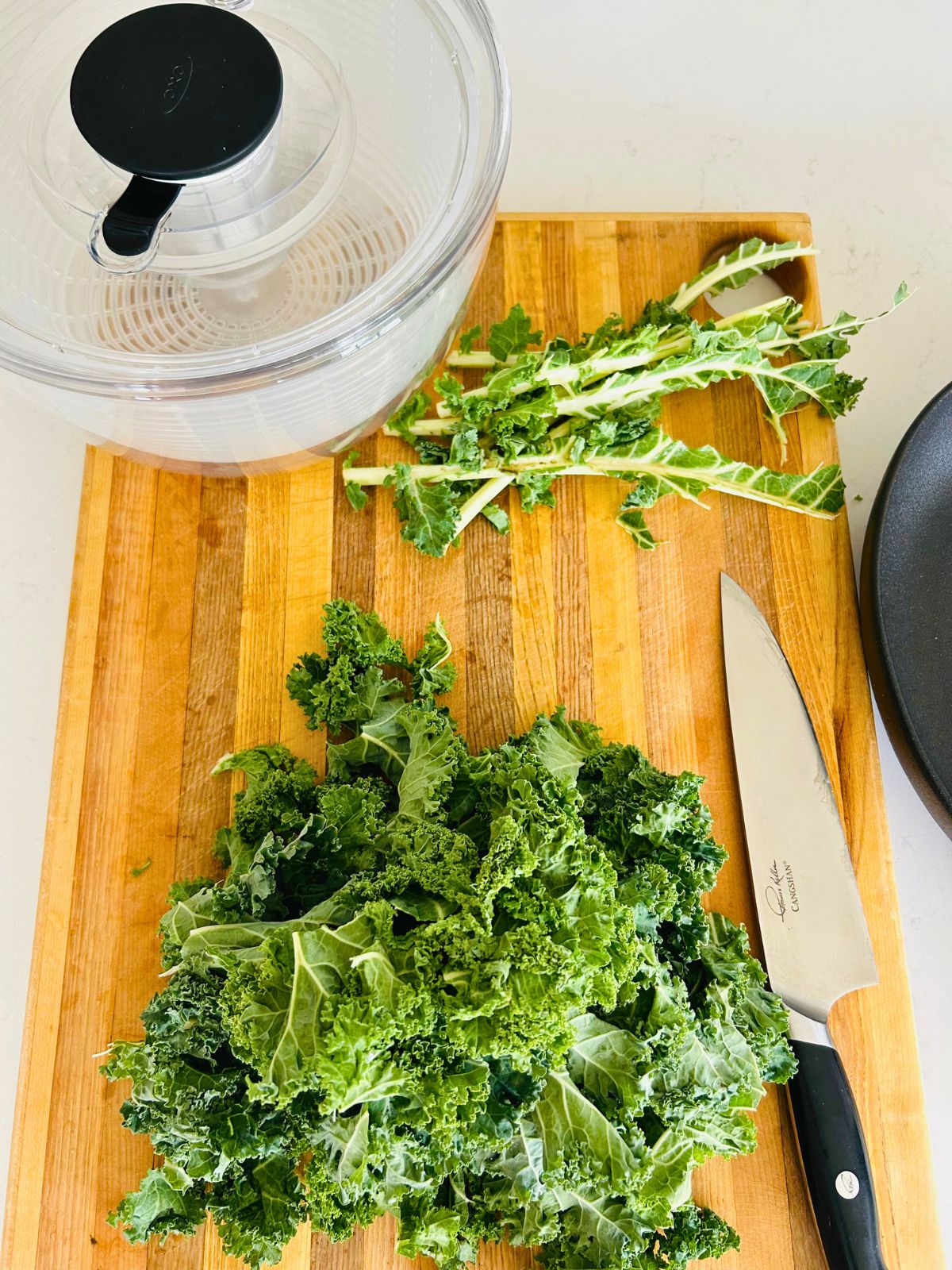Kale leaves and their stems next to a salad spinner.