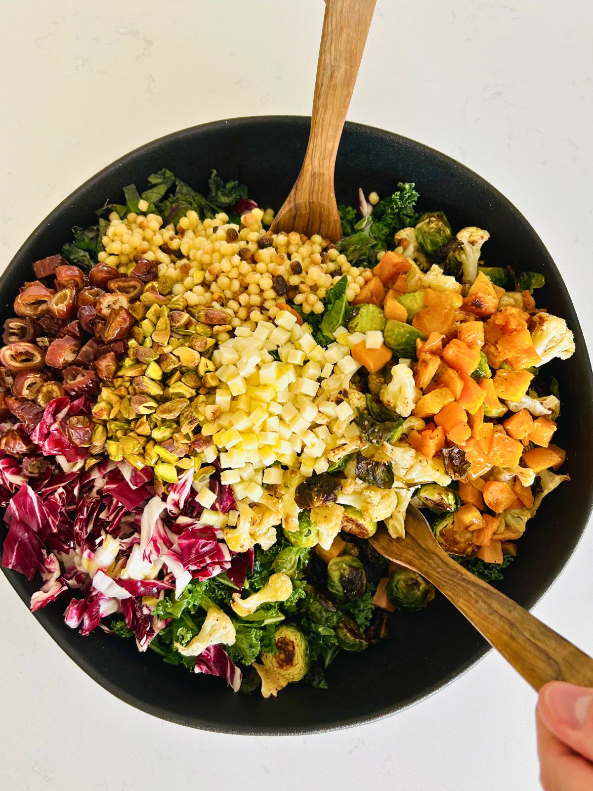 Seasonal vegetable salad in a large bowl with salad tongs starting to mix it.