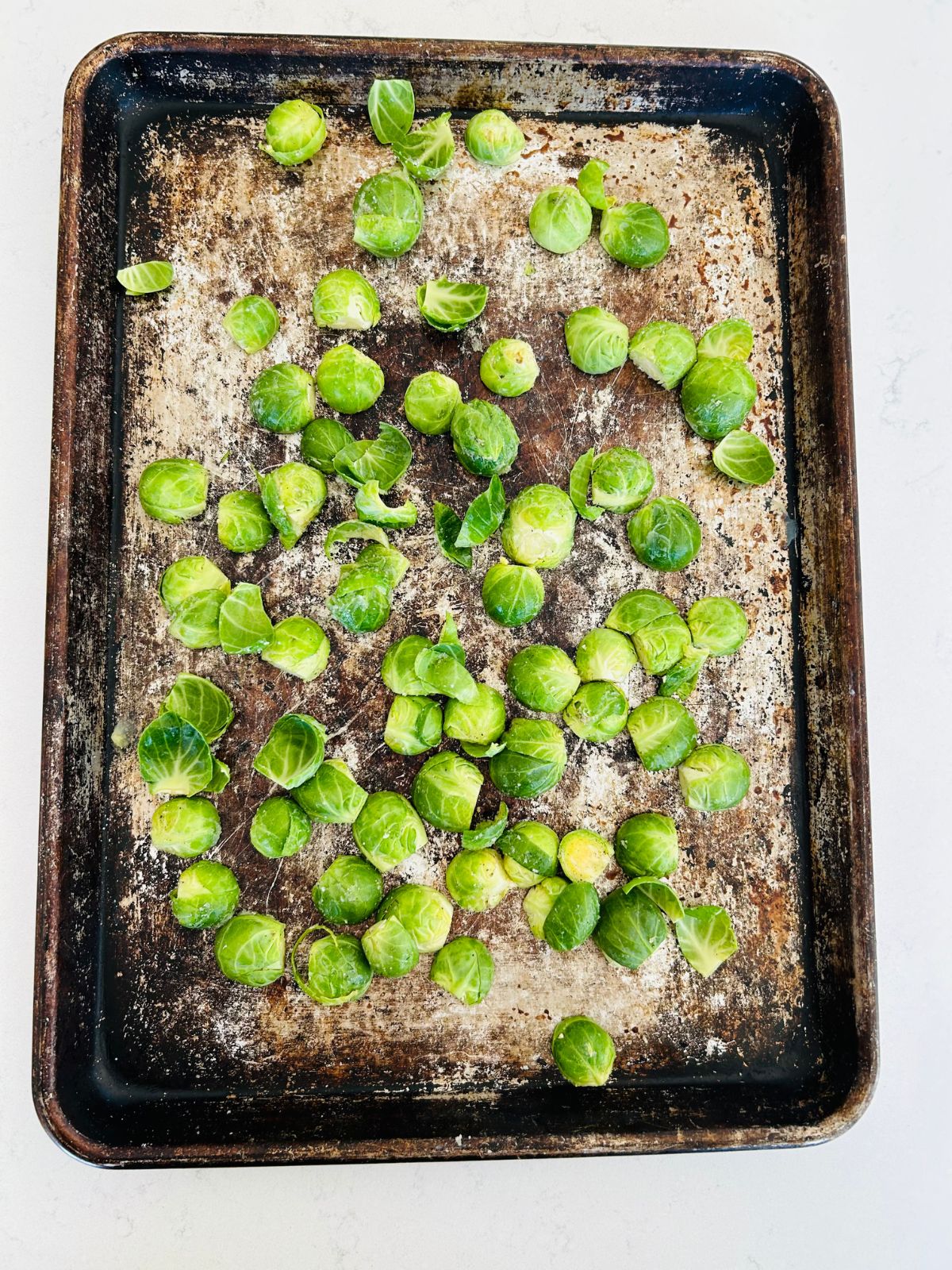 A cookie sheet of raw Brussels sprouts that have been cored, halved, and seasoned.