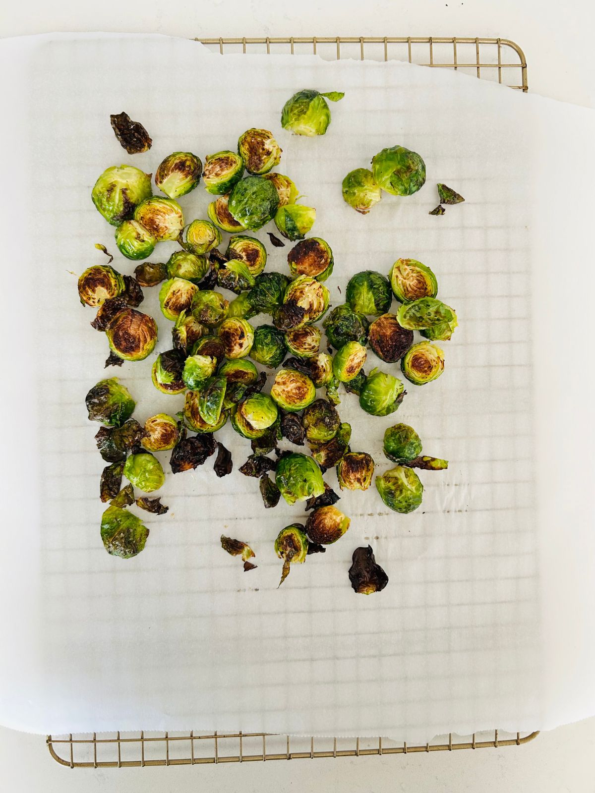 Roasted and caramelized Brussels sprout halves cooling on a parchment lined cooling rack.