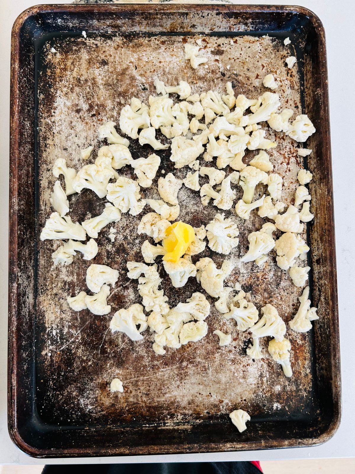 Raw, bite-sized cauliflower florets with ghee on a cookie sheet before roasting.
