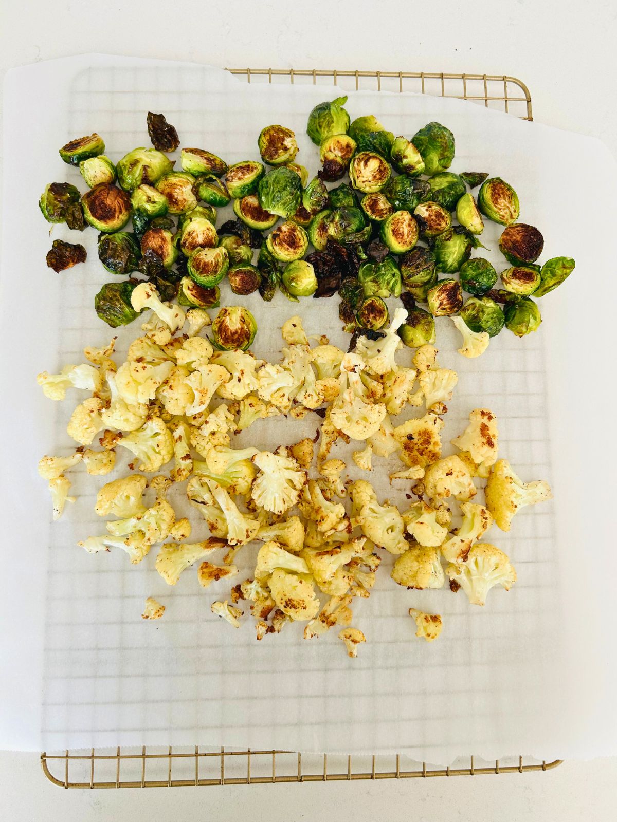 Roasted Brussels sprout halves and cauliflower florets on a lined metal cooling rack.