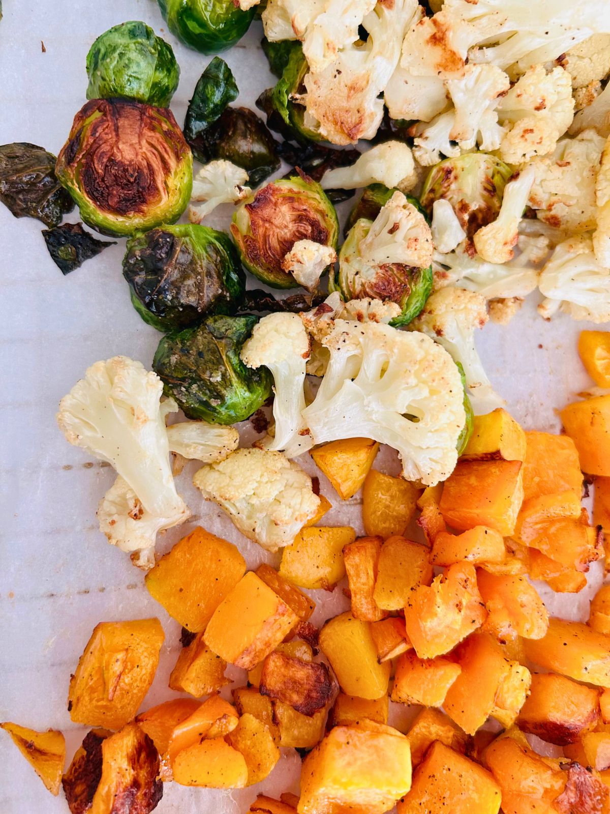 Roasted Brussels sprout halves, cauliflower florets, and cubed butternut squash on a cooling rack.