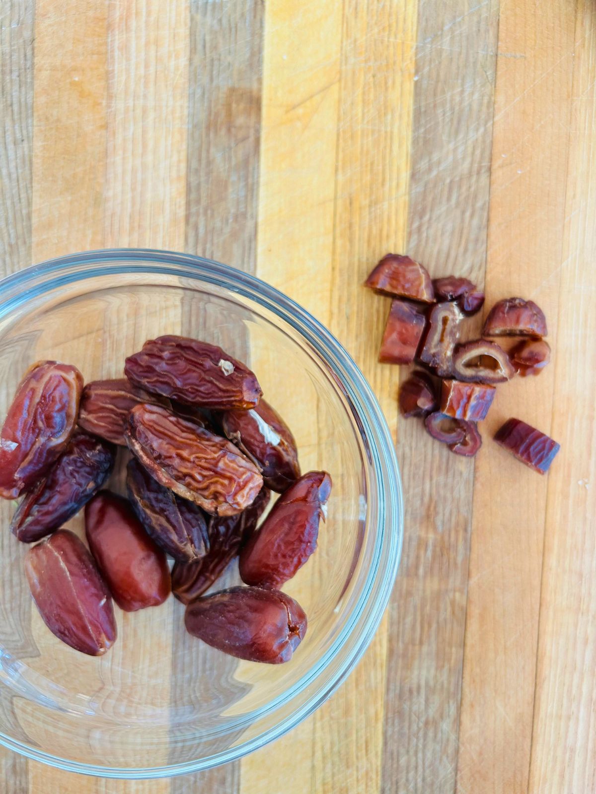 A bowl of whole dried dates next to dates that have been sliced into quarters on a cutting board.