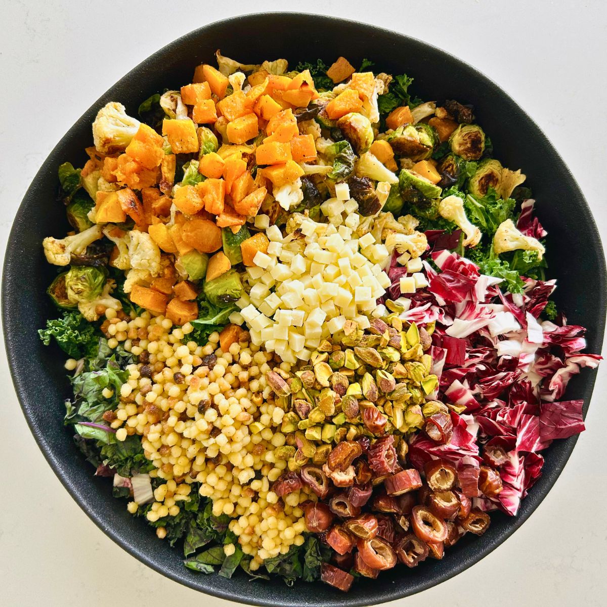 Roasted seasonal vegetable salad in a black bowl before tossing with white balsamic vinaigrette.