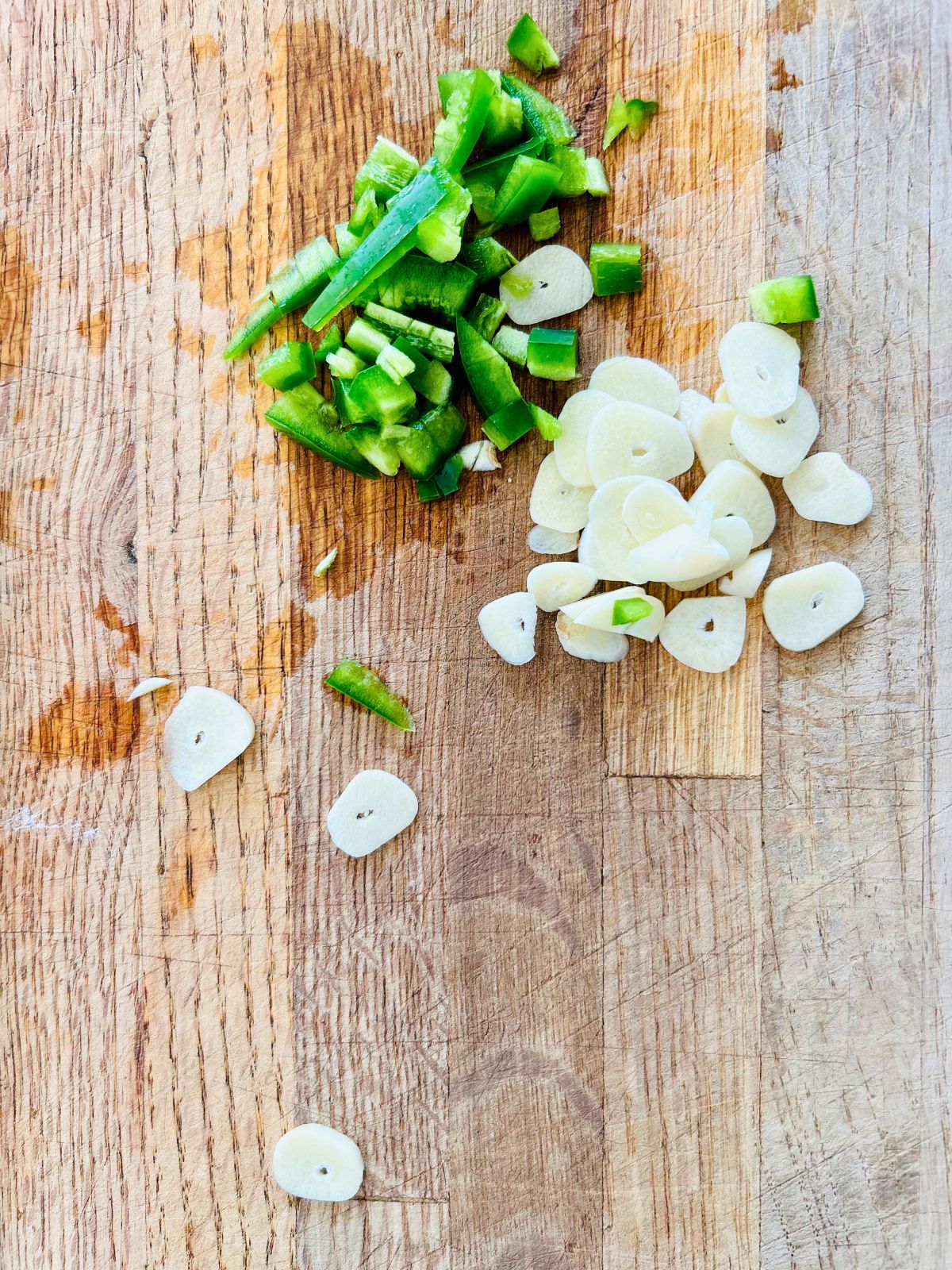 A chopped jalapeno and garlic cloves on a cutting board.