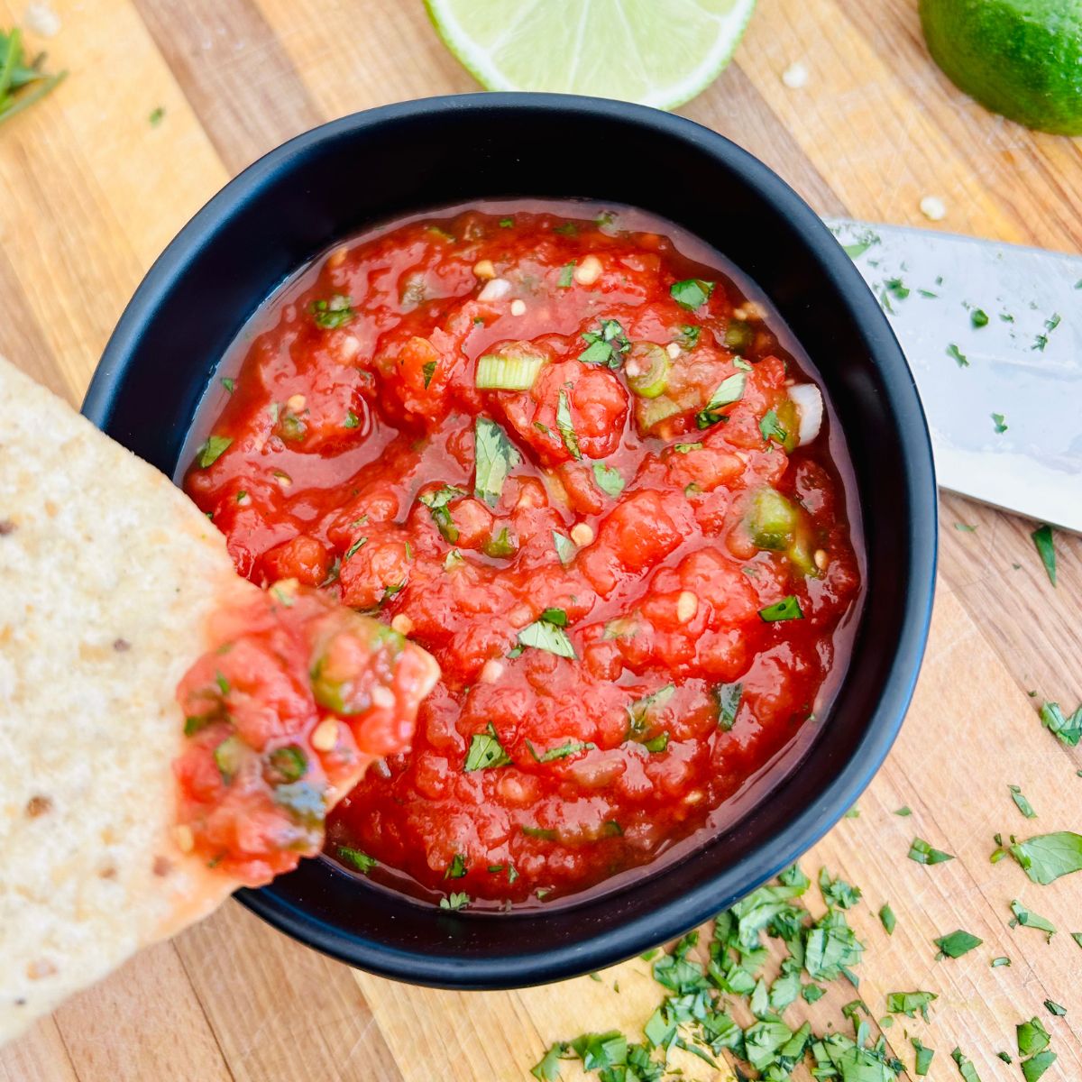 A tortilla chip dipped in salsa and held over the bowl.