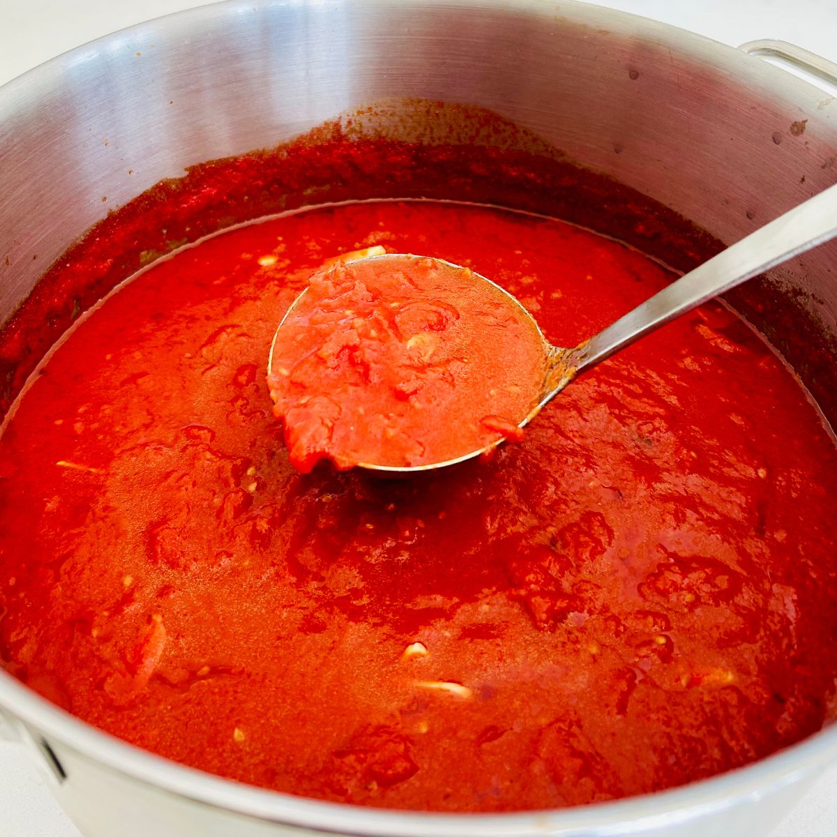 Marinara sauce in a large pot with a metal ladle scooping up a portion.