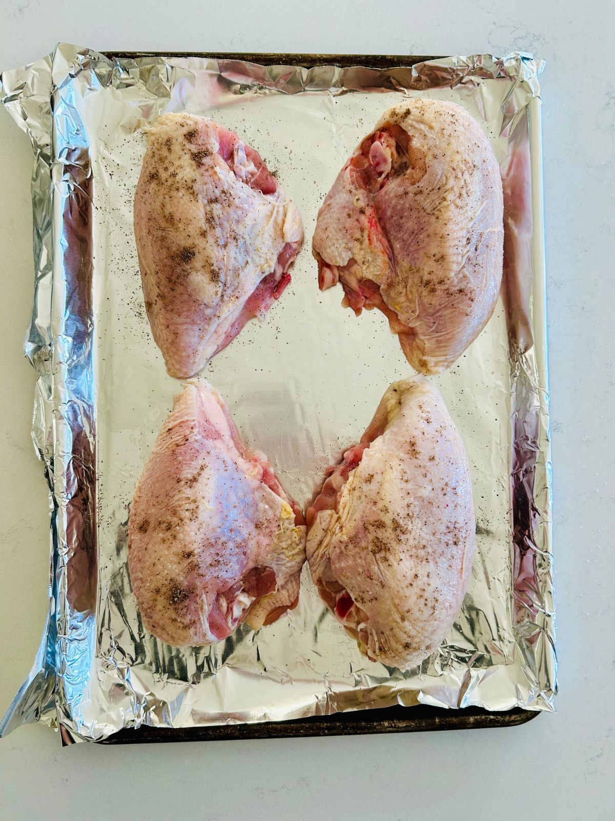 Seasoned, raw split chicken breasts on a foil lined cookie sheet.