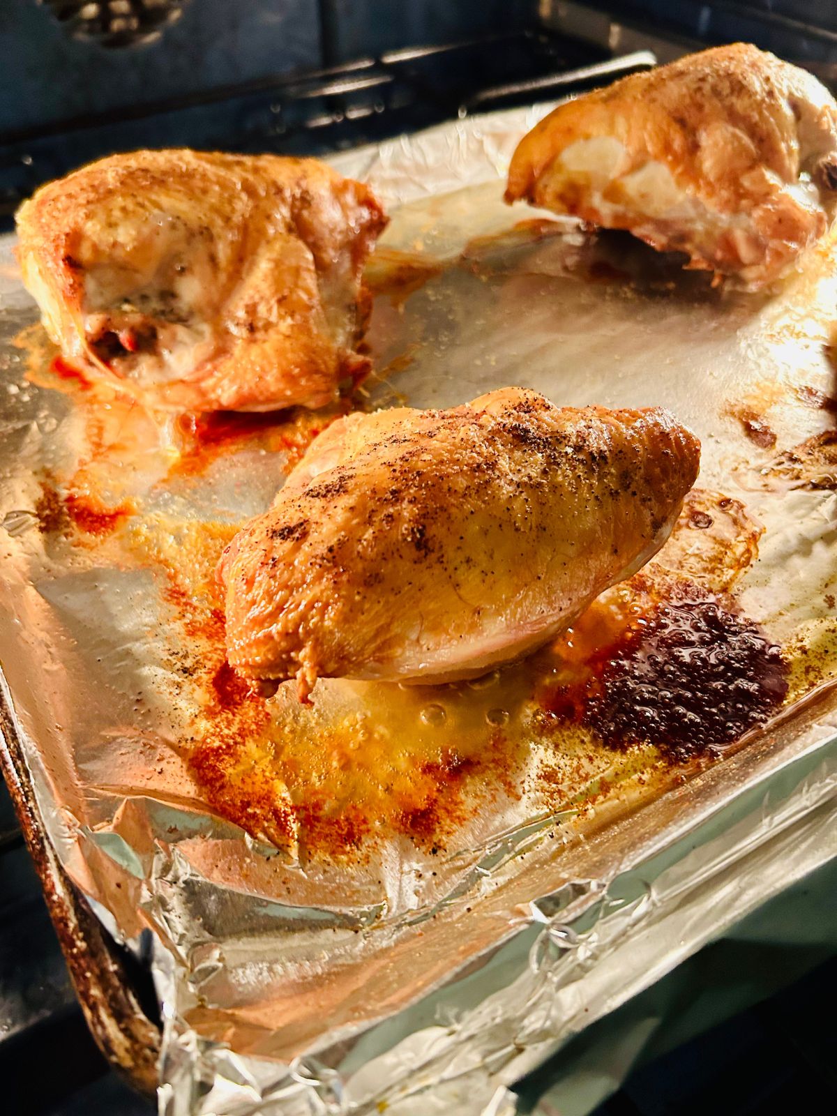 Roasted bone-in split chicken breast on top of a foil lined sheet pan inside the oven.