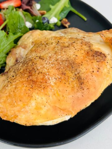 Sheet pan bone-in chicken breast next to a salad on a black plate.