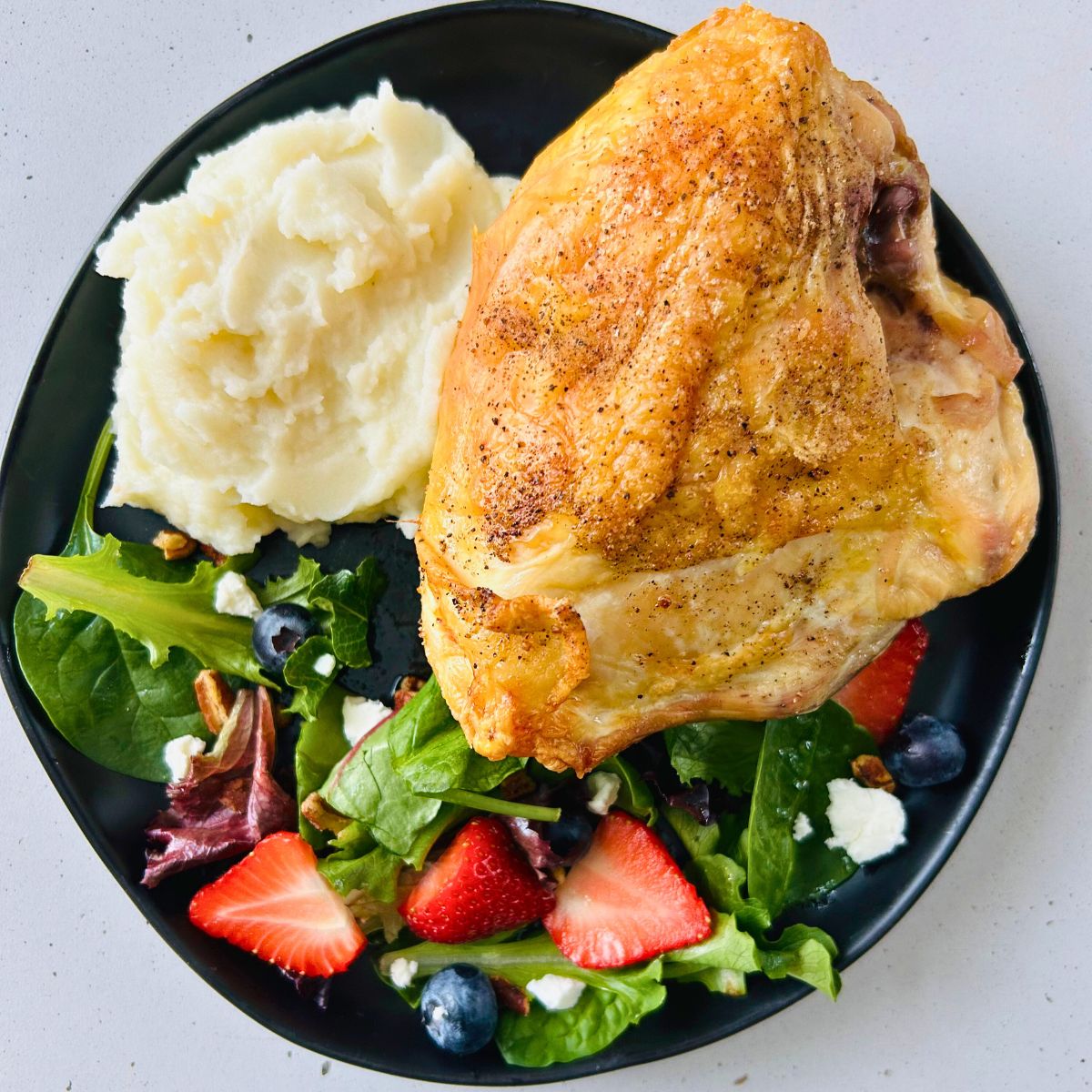 Sheet pan bone-in roasted chicken breast with a berry salad and mashed potatoes on a black plate.