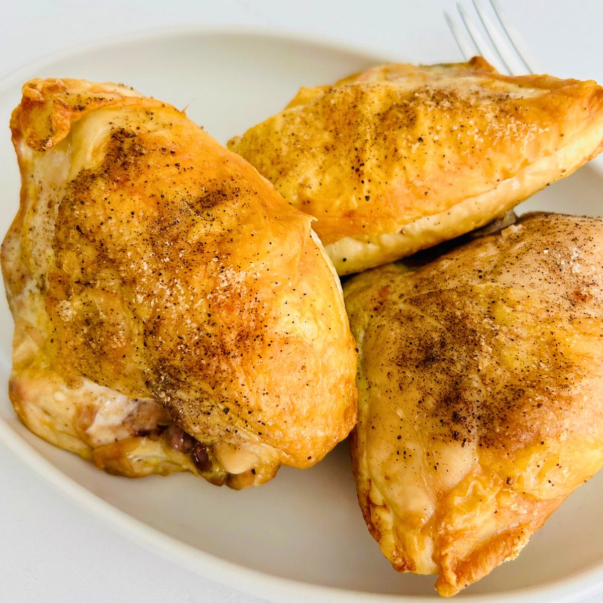 Three roasted bone-in skin-on chicken breasts on a white oval platter.