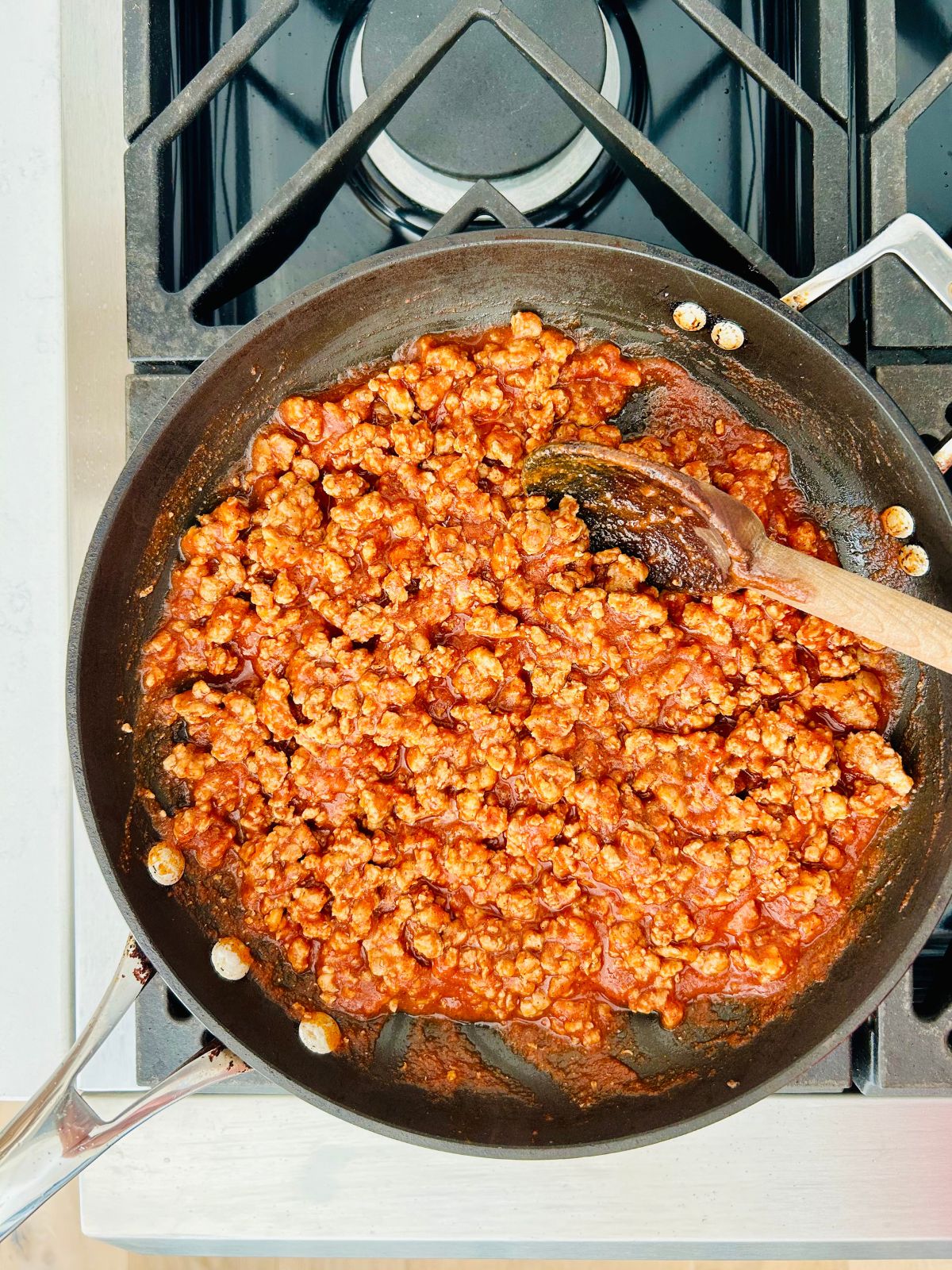 Cooked ground meat in a skillet with taco seasoning and tomato sauce added to it.