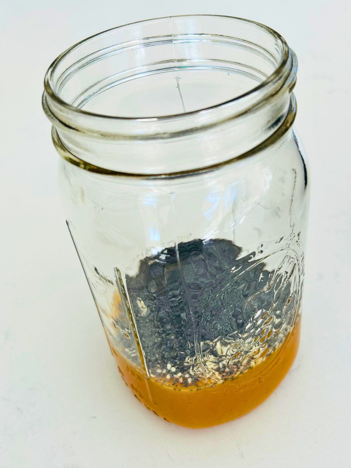 Strawberry spinach salad's apple cider vinaigrette is in a mason jar with sesame and poppy seeds added on top.