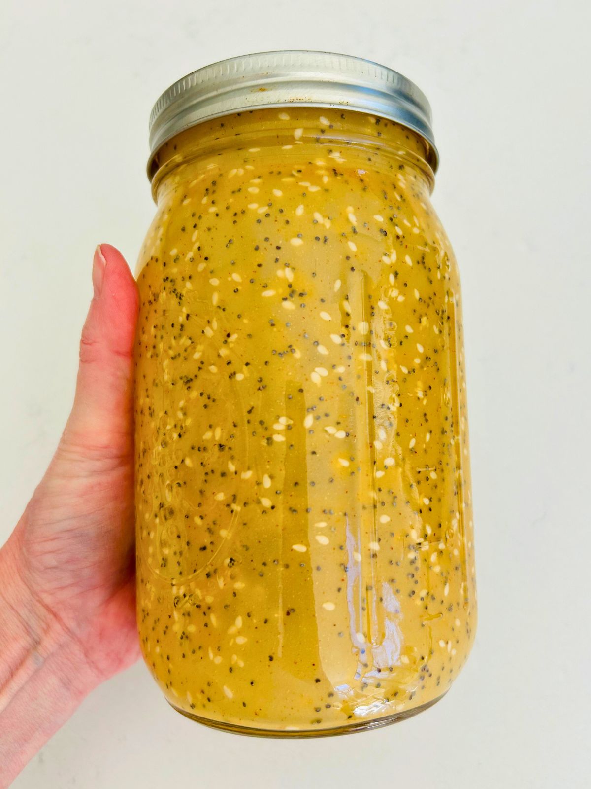 Apple cider vinaigrette is combined with poppy and sesame seeds in a mason jar.