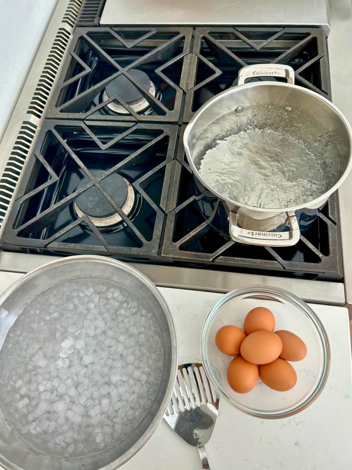 A pot of rapidly boiling water, a bowl of icy water, 6 eggs, and a slotted spoon ready to boil eggs.