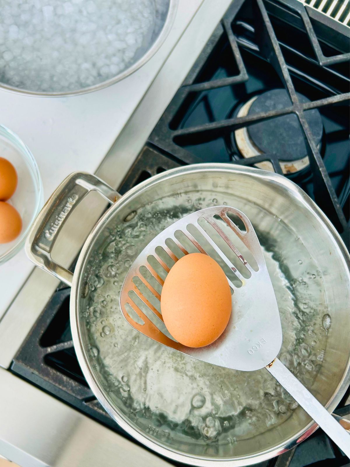 A fresh egg in a slotted spoon getting ready to go into the pot of boiling water.