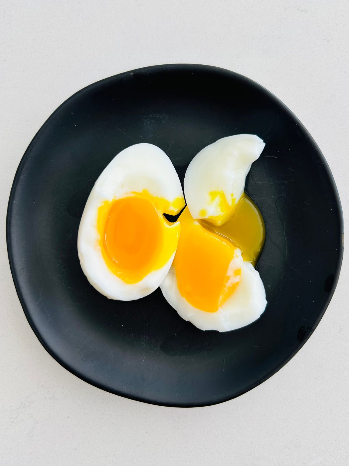 A quick and easy soft boiled egg split open on a black plate.