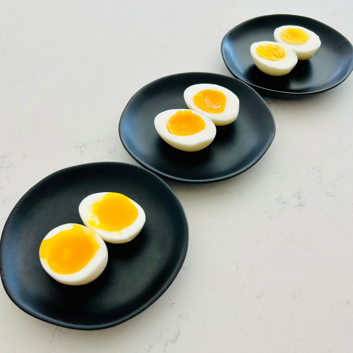 Soft, medium, and hard boiled eggs split open on black plates.