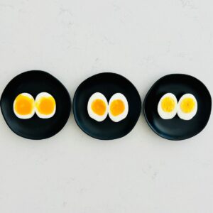 Soft, medium, and hard boiled eggs split open on small black plates.