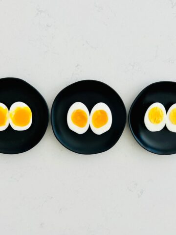 Soft, medium, and hard boiled eggs split open on small black plates.