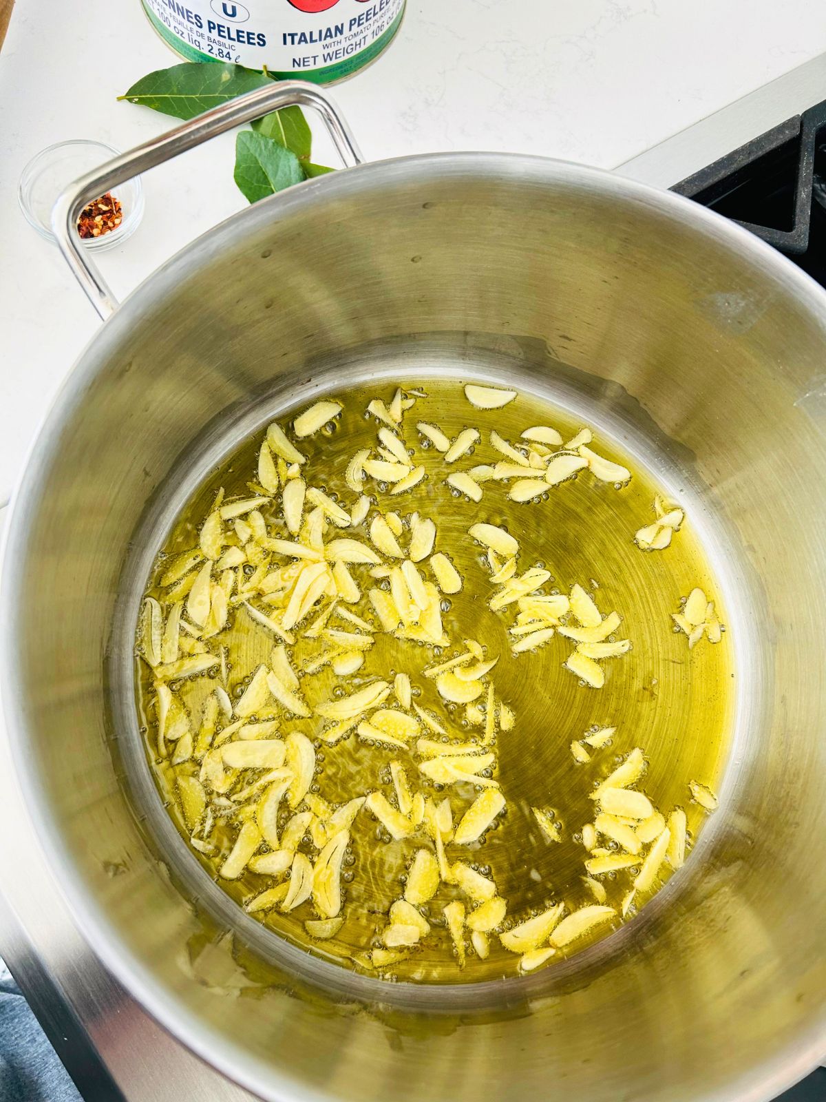 Sliced garlic is simmering in hot olive oil.