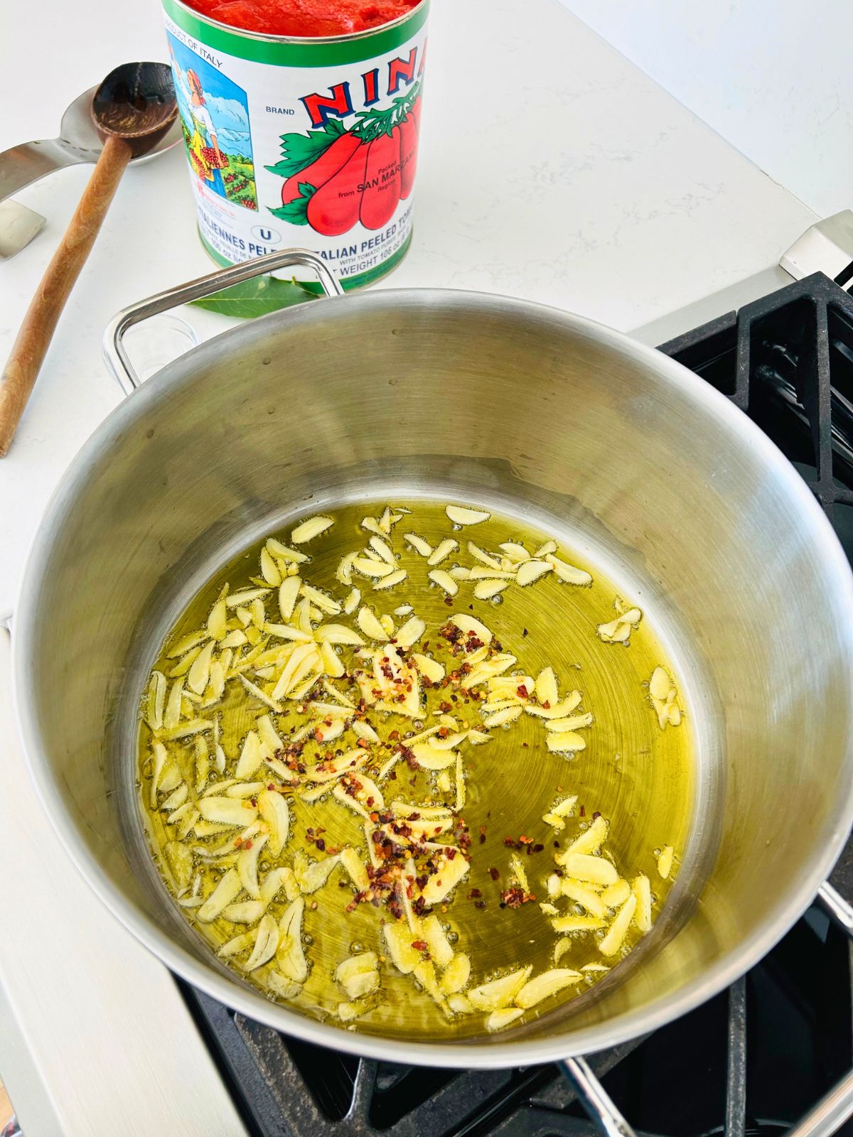 Sliced garlic cloves and red pepper flakes simmering in a pot of olive oil.