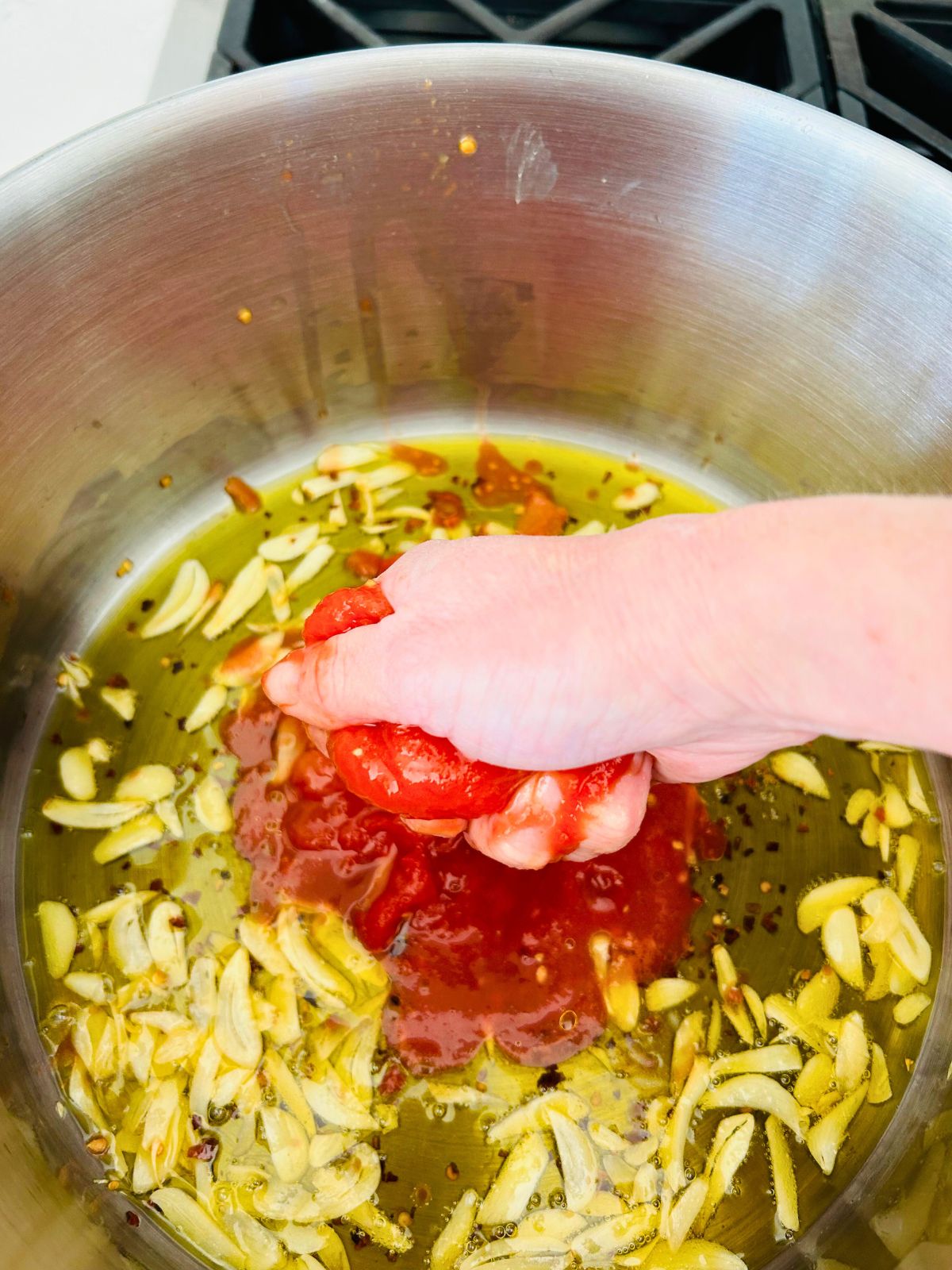 Hand crushing whole peeled tomatoes into the hot olive oil with garlic and chili pepper flakes.