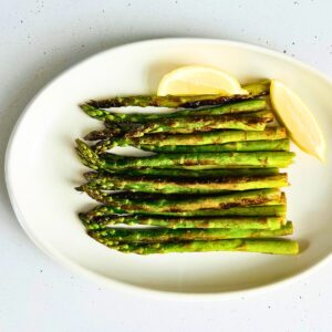 Sauteed asparagus with lemon on a white oval plate.