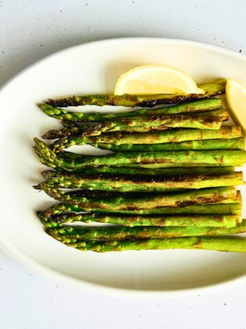 Sauteed asparagus with lemon on a white oval plate.