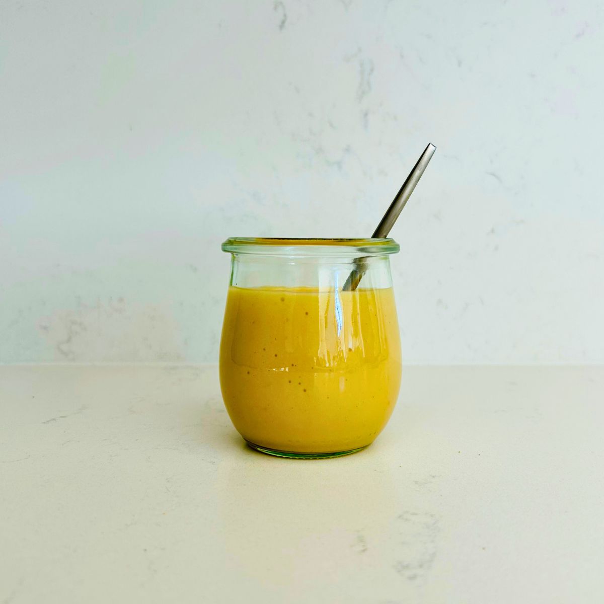 Honey mustard dressing in a clear mason jar with a spoon resting in it.