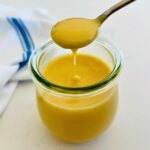 A spoonful of honey mustard salad dressing dripping over a jam jar.