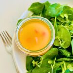 Hot bacon salad dressing next to spinach on a plate.