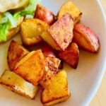 Pan roasted baby potatoes next to a burger on a white plate.