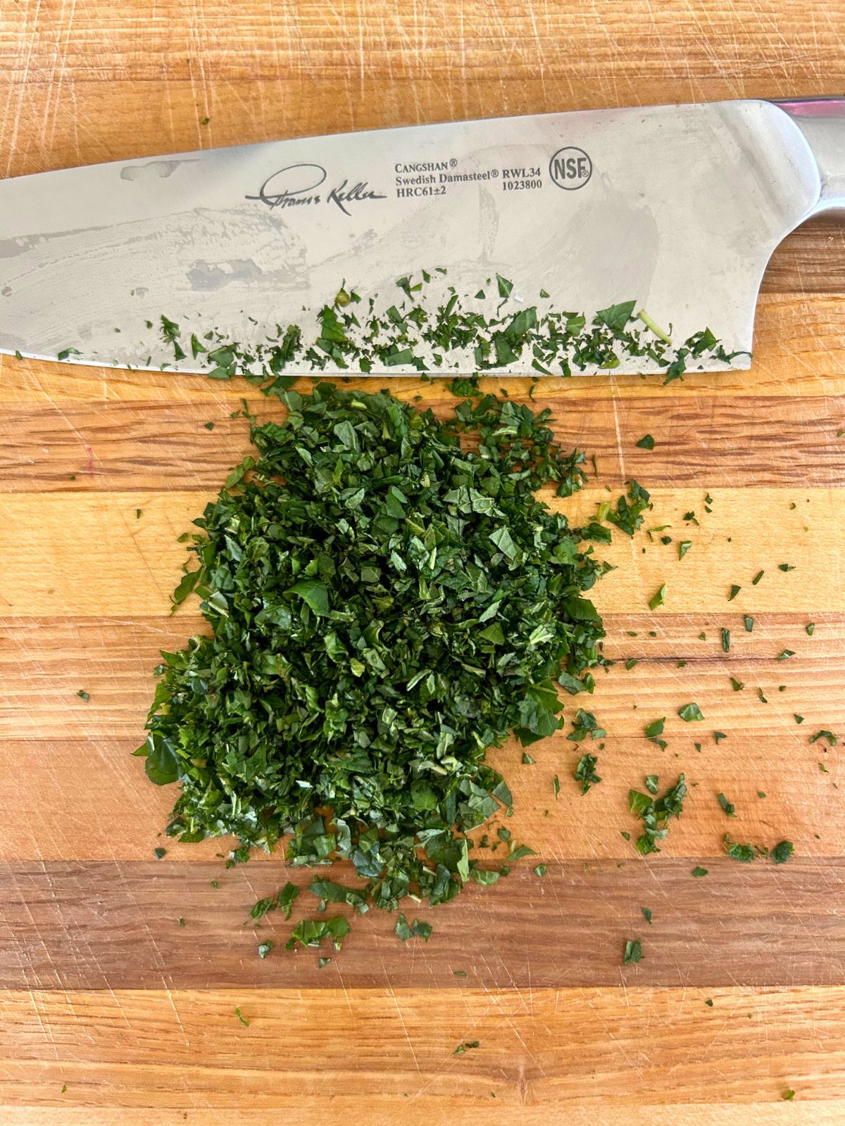 Finely chopped fresh mint leaves with a little bit of salt next to a knife on the cutting board.