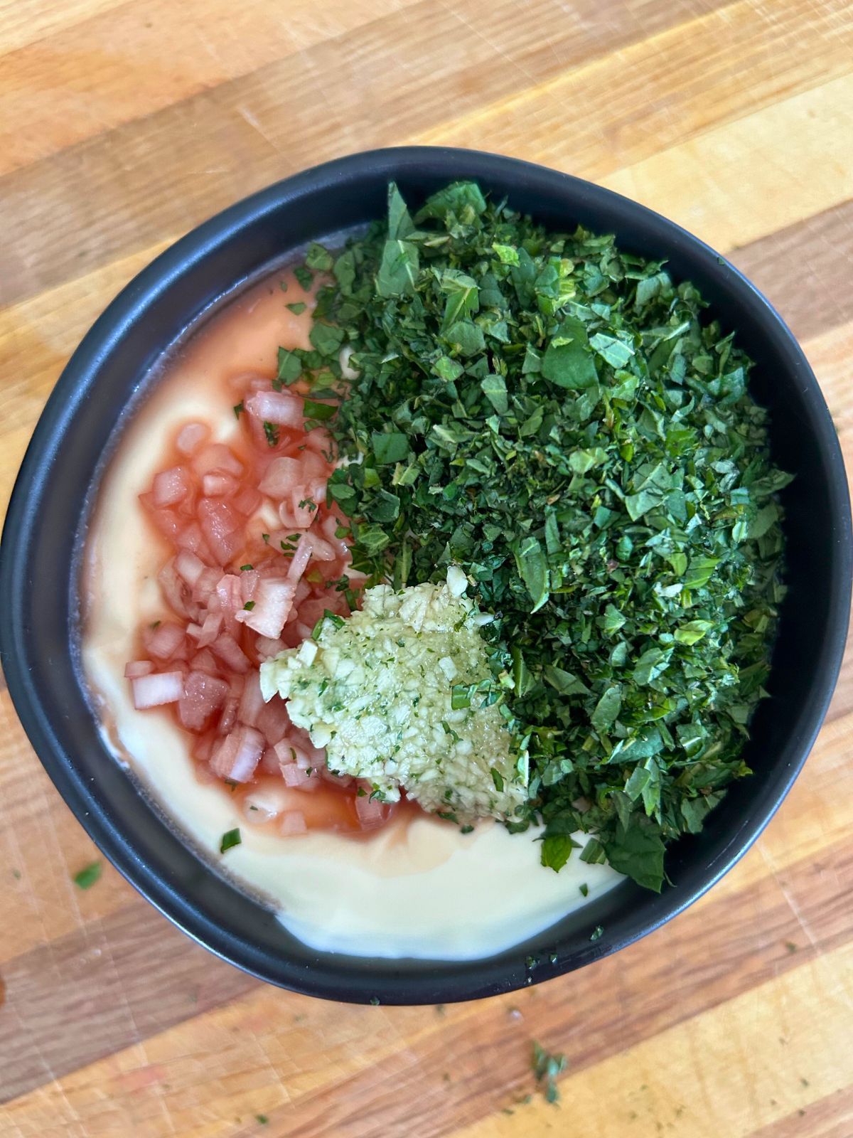 Shallots, garlic paste, and finely chopped mint on top of a bowl of creme fraiche.