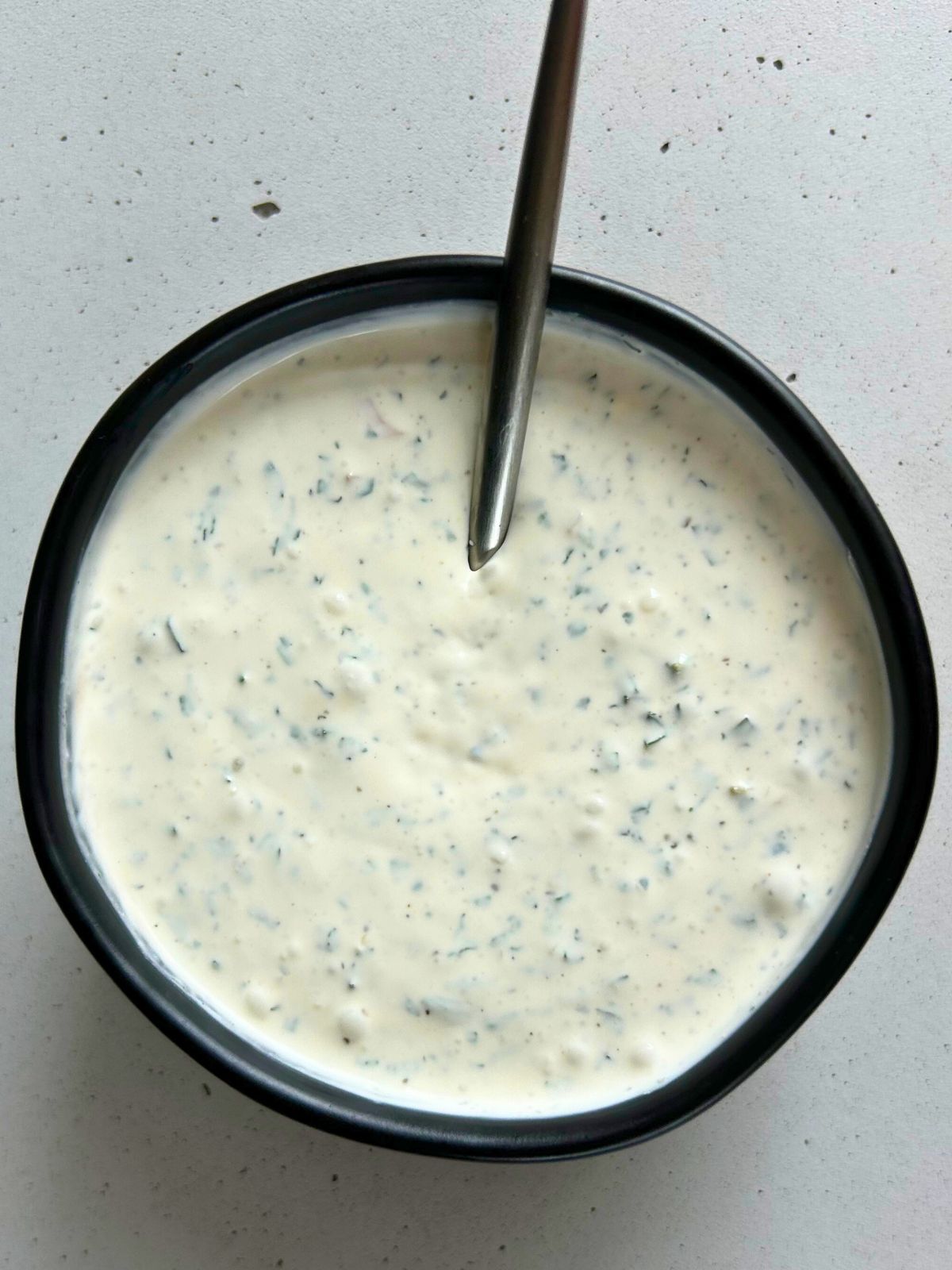 A small black bowl of mint creme fraiche with a spoon.