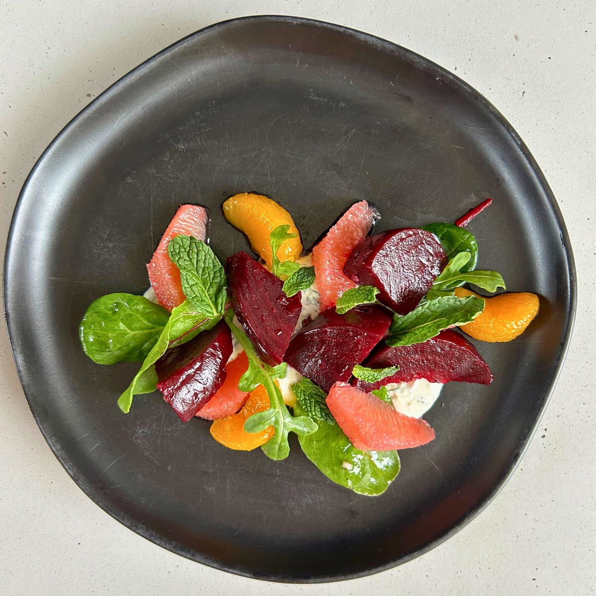 Roasted beet salad with citrus and creme fraiche on a black plate.