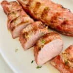 Slices of gas-grilled pork tenderloins with salt and pepper on a white plate.