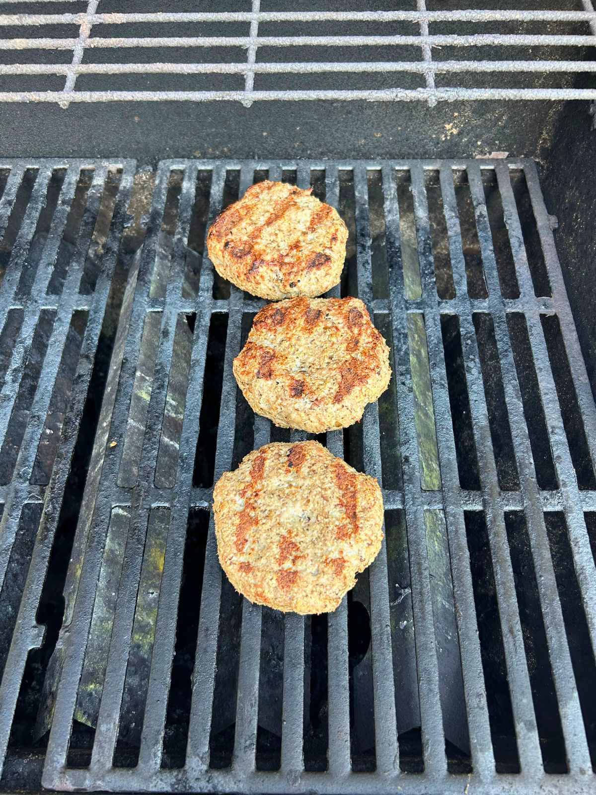 Turkey burgers with mushrooms have flipped to their other side on the grill.