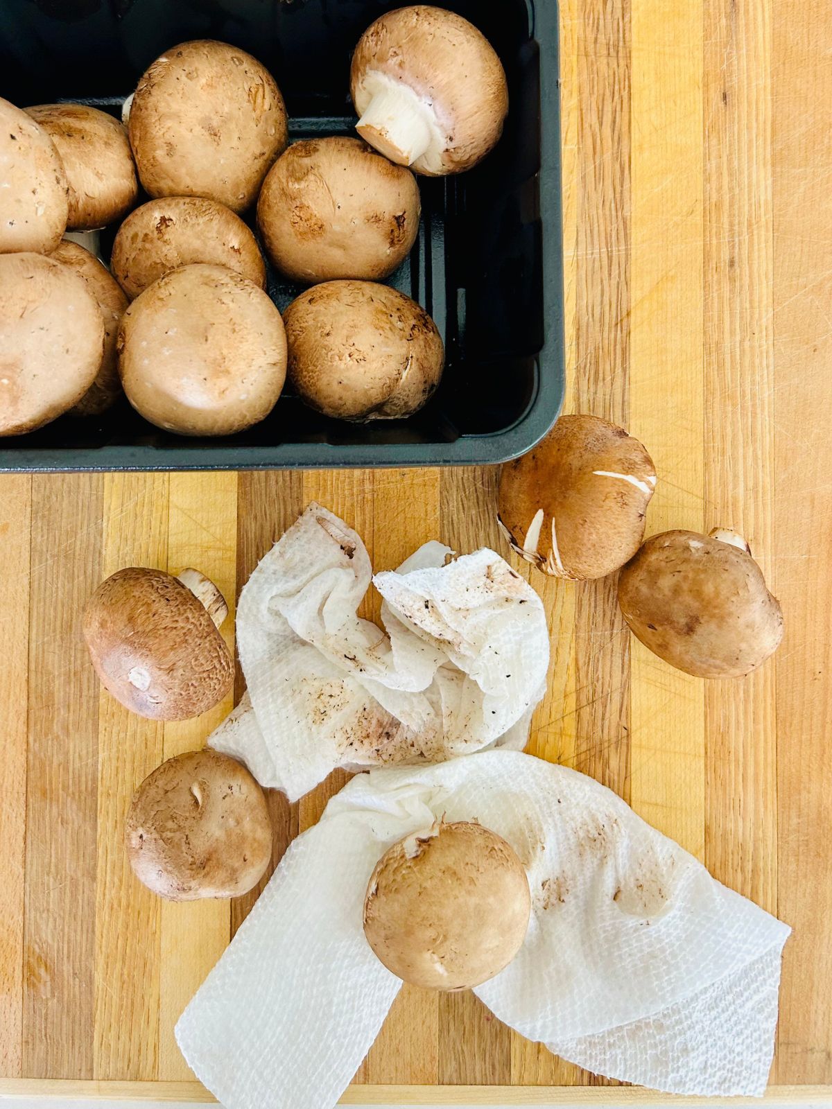 A cutting board with dirty and damp paper towels and clean portobello mushrooms.