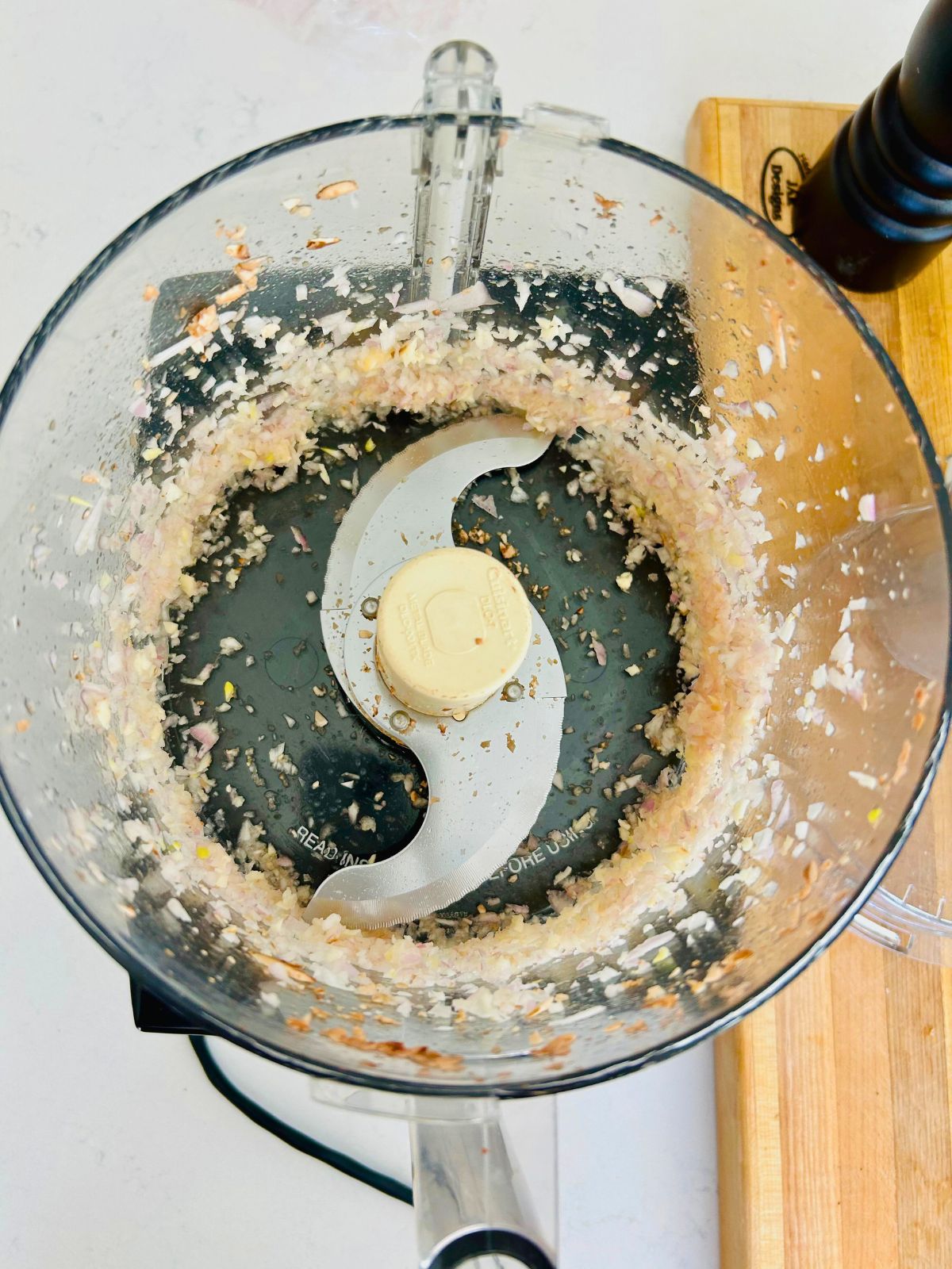 Minced shallots and garlic inside a food processor bowl.