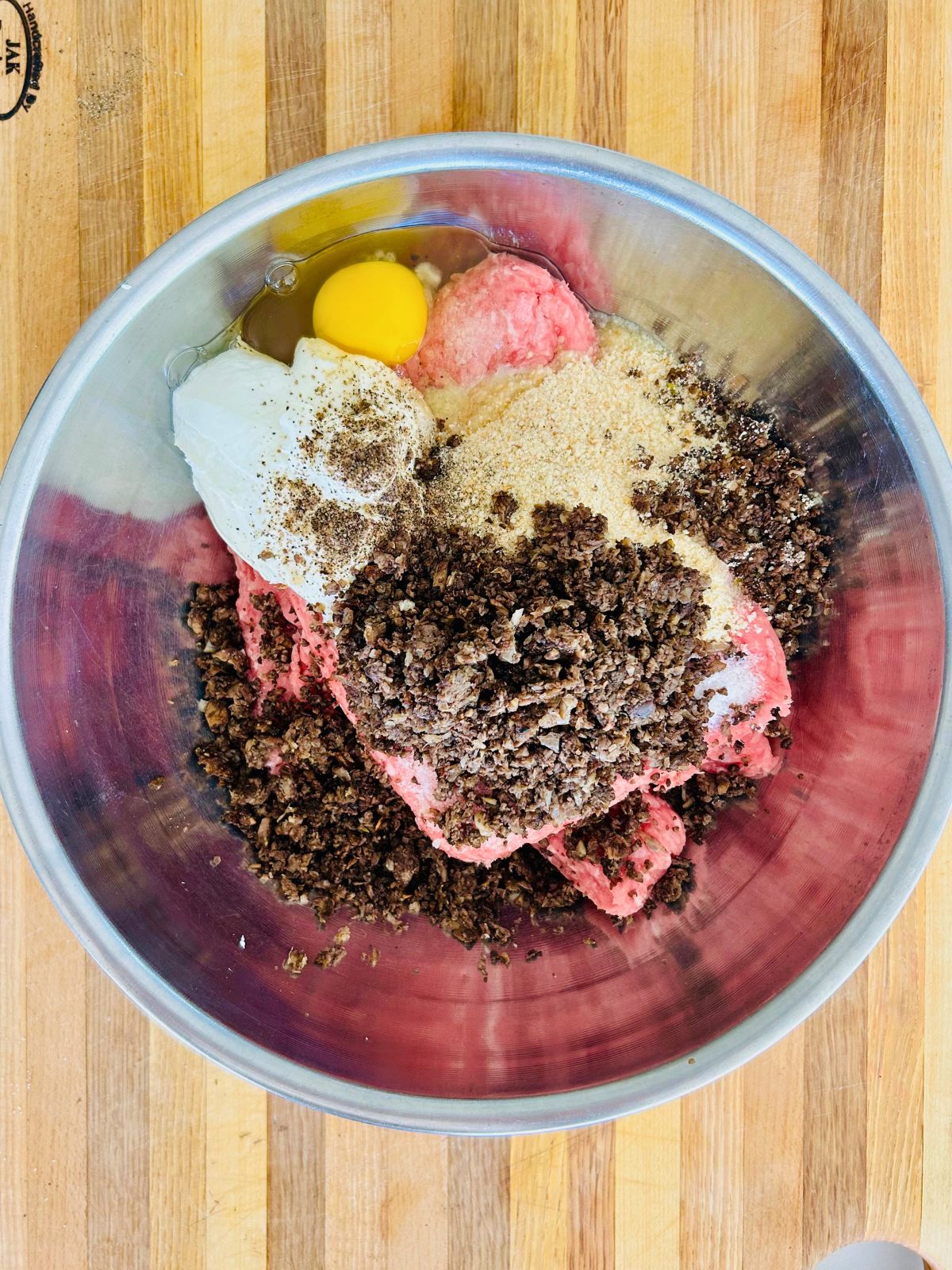Ground turkey, cooked mushrooms, egg, yogurt, and breadcrumbs needed to make a turkey burger in a metal mixing bowl.